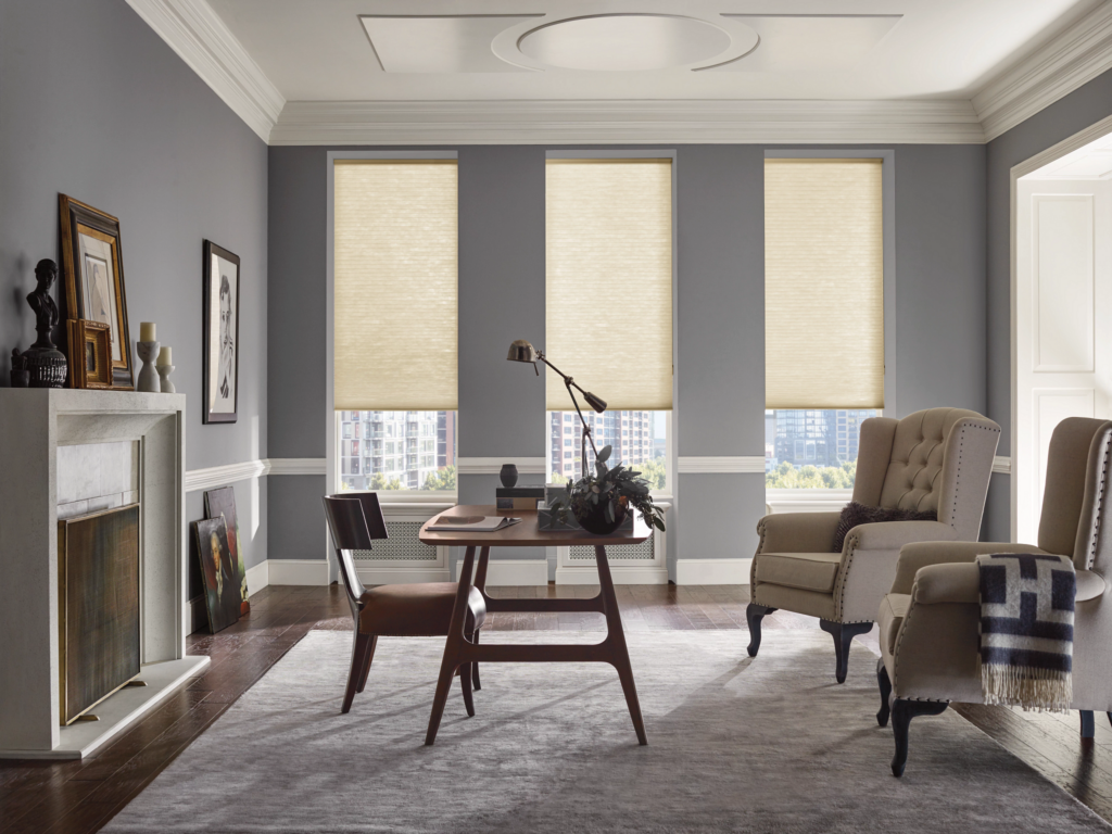 A sophisticated home office with motorized light-filtering honeycomb shades on tall windows, a desk, armchairs, and artwork.